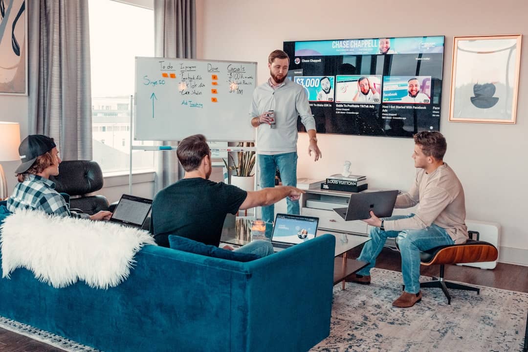 Team collaborating in a modern office with laptops, video conferencing on a TV, and a whiteboard, illustrating hybrid and remote team building.