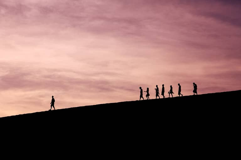 Silhouettes of people walking uphill against a pink sky, symbolizing leadership and teamwork for hybrid and remote recruitment strategies.