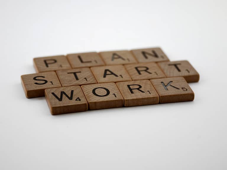Wooden letter tiles spell out "PLAN," "START," and "WORK," emphasizing key steps for effective hybrid work management strategies.
